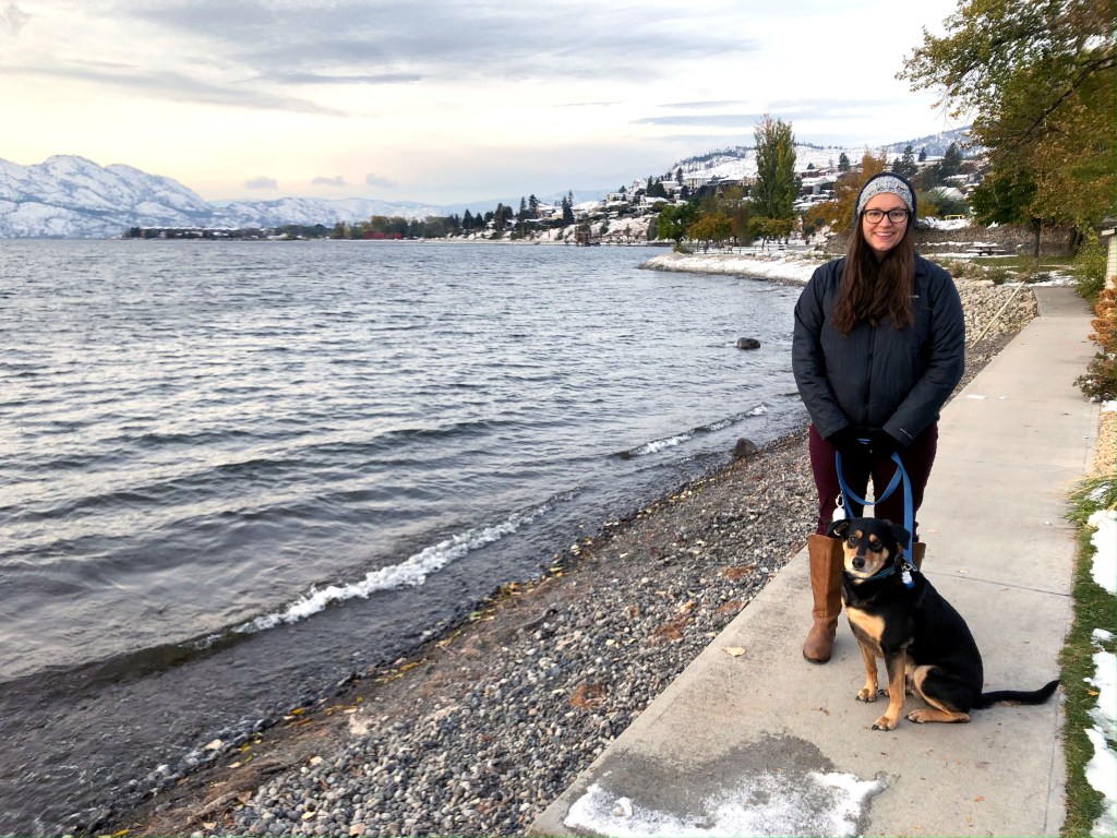 Woman and a dog standing beside a lake with snow on the ground